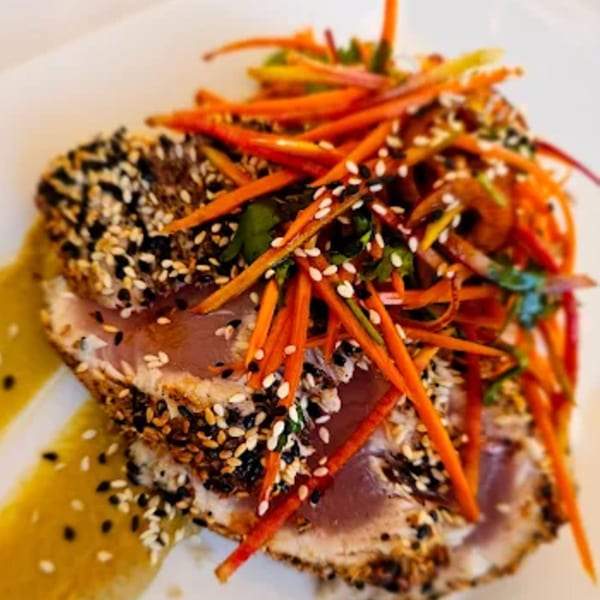 Seared tuna slices crusted with sesame seeds, topped with julienned carrots and a yellow sauce.
