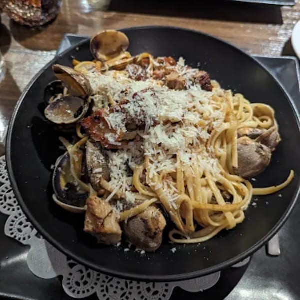 Linguine pasta with clams, seafood, and grated cheese in a black bowl on a white doily.