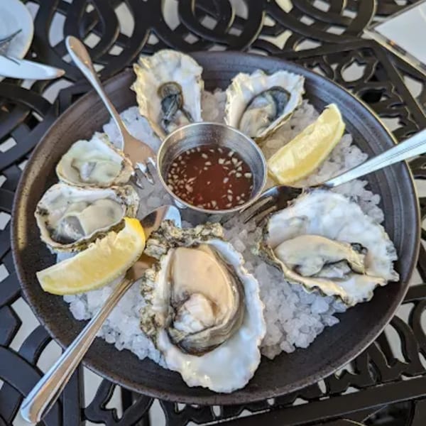 A platter of fresh oysters on ice with lemon wedges and a dipping sauce at KW Saltwater Grill.