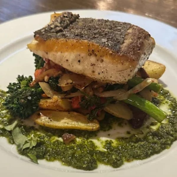 KW Saltwater Grill's pan-seared fish with roasted vegetables and green pesto on a white plate.