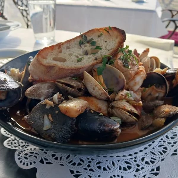 A large bowl of seafood stew with mussels, clams, and shrimp, topped with a slice of bread.